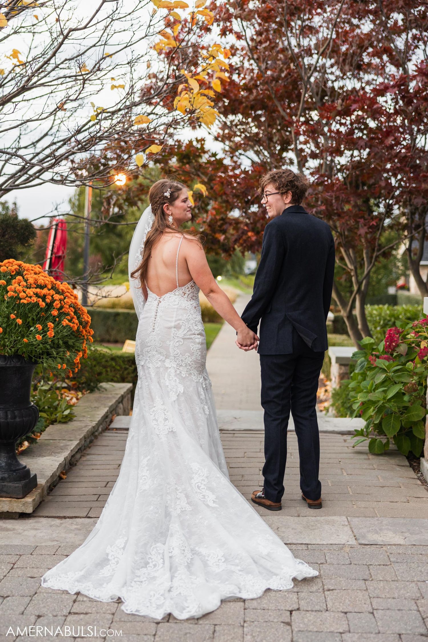 Bride and groom walking hand in hand on stone path surrounded by fall flowers.