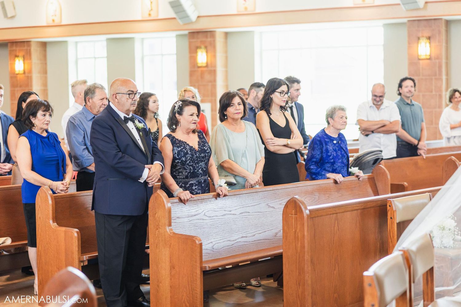 Wedding guests stand in wooden pews during a church ceremony.