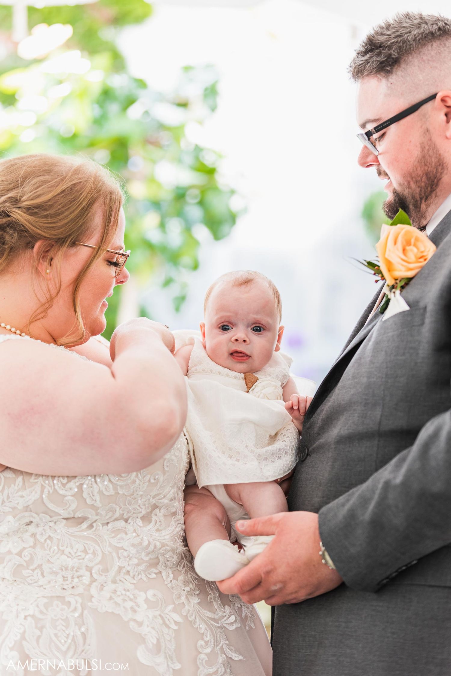 Sweet moment with a baby in white dress during outdoor wedding celebration.