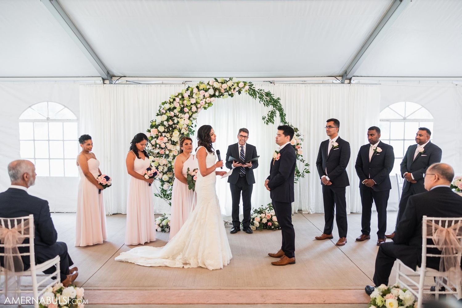 Wedding ceremony in progress under a beautiful floral arch with bridesmaids and groomsmen.