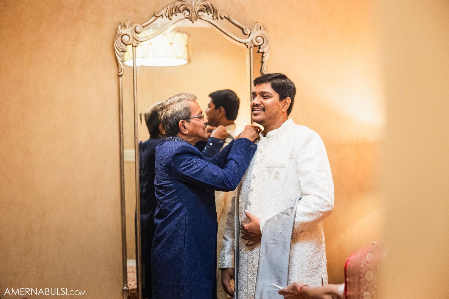 A pre-wedding preparation scene with traditional attire adjustments in front of an ornate mirror.