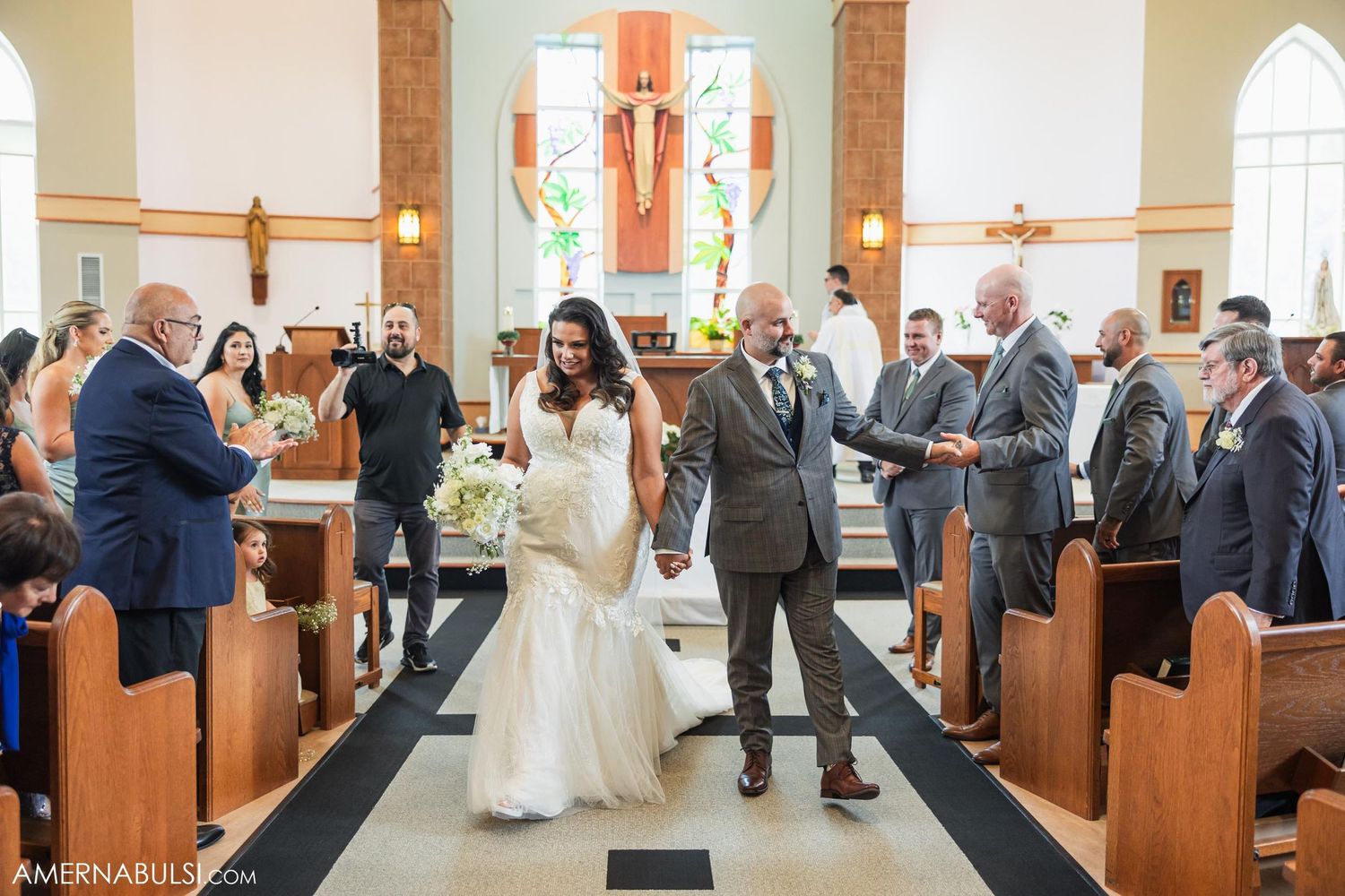 Wedding celebration in church with guests standing in wooden pews.