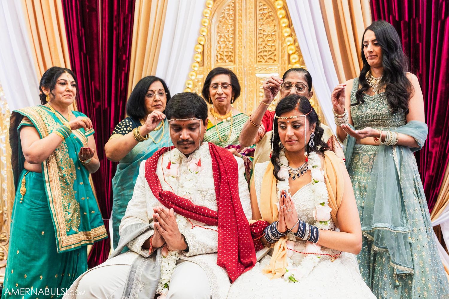 Wedding guests in colorful saris surround the couple during a celebratory ceremony moment.