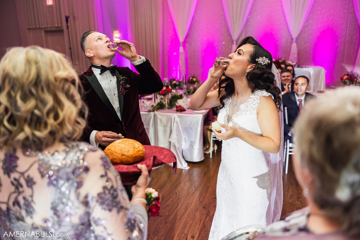 Wedding reception celebration with traditional bread ceremony under pink ambient lighting.
