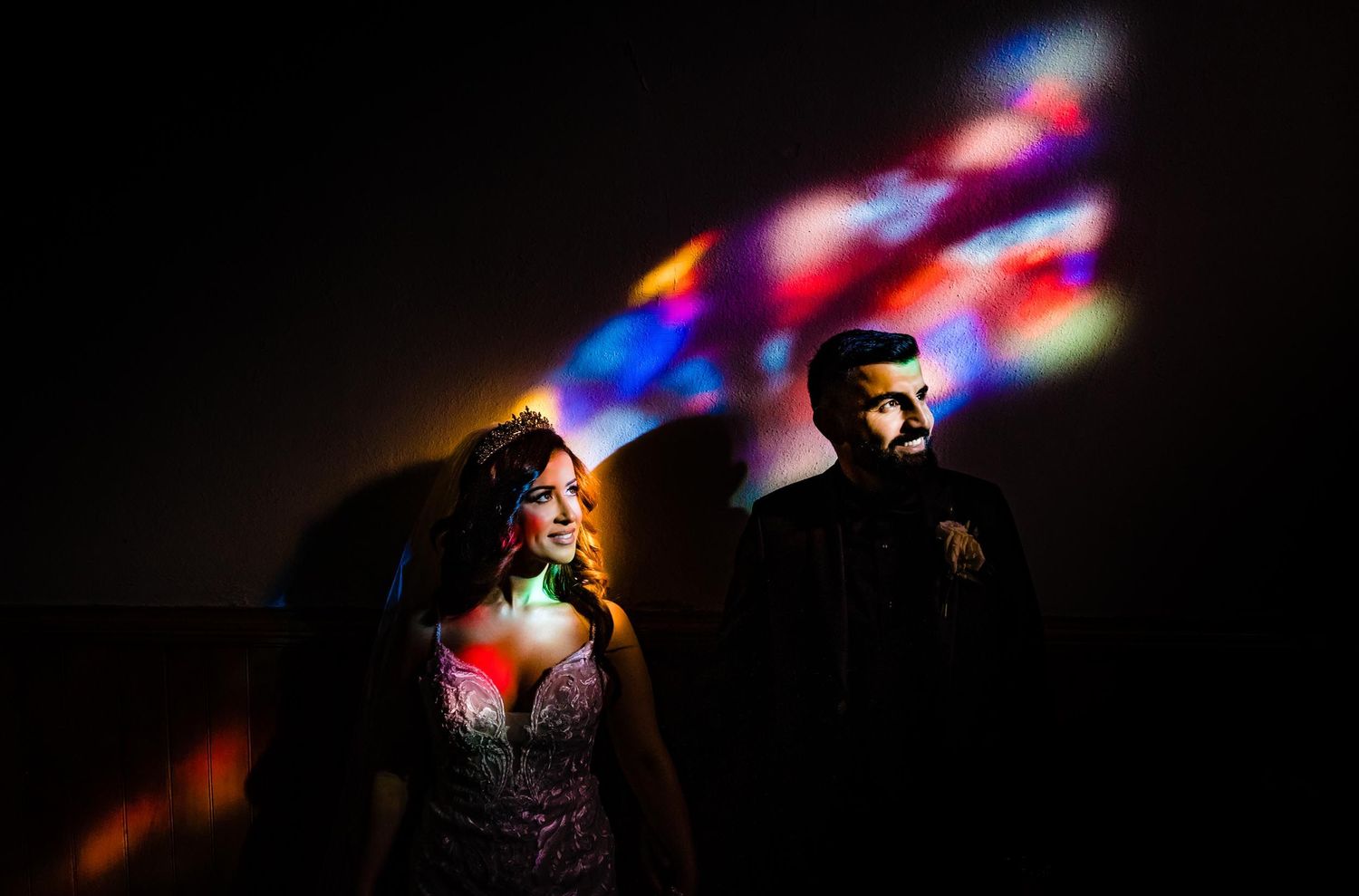 Artistic silhouette with colorful light projections creates romantic wedding portrait.