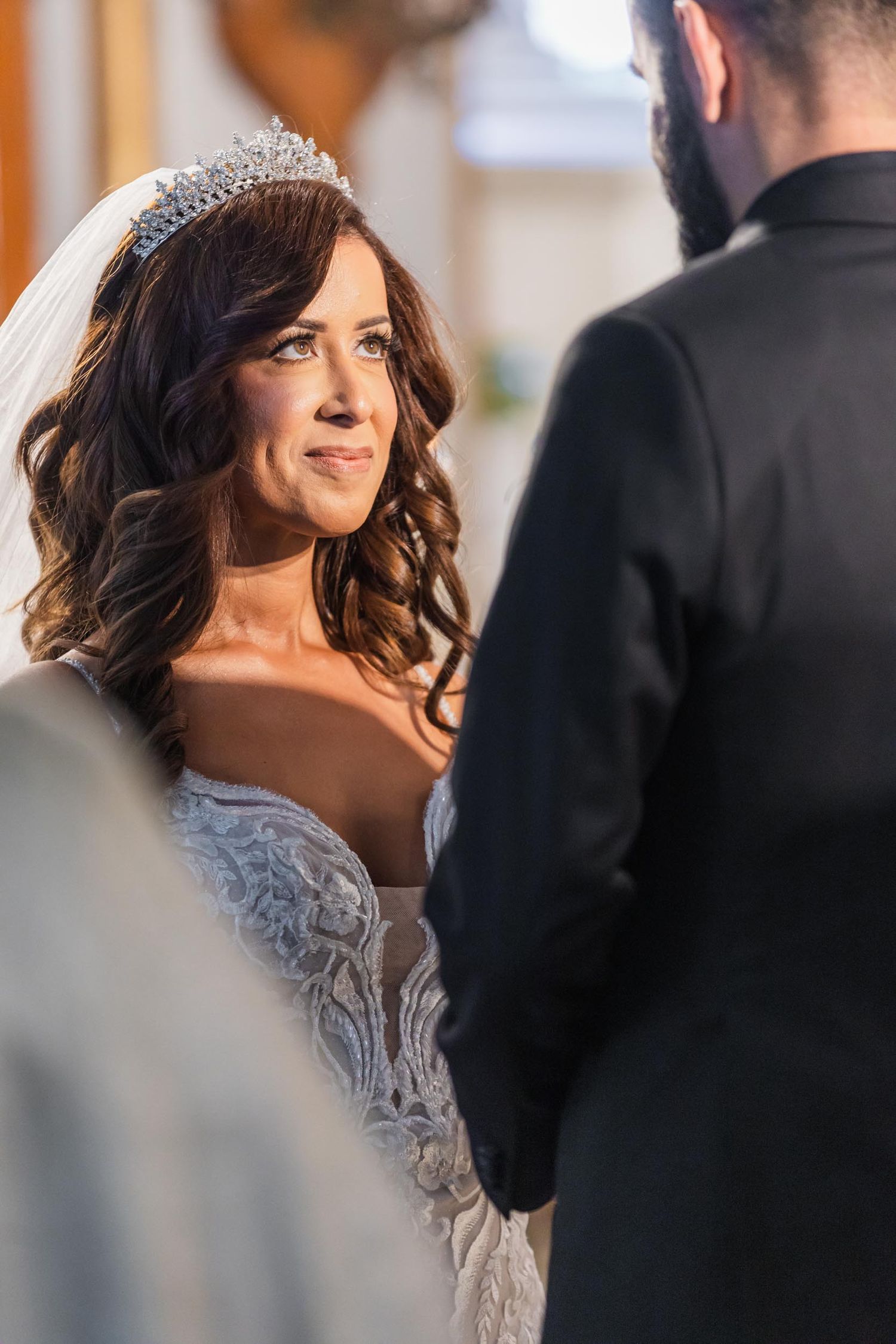 A bride in a lace wedding gown and tiara looks lovingly during the wedding ceremony.