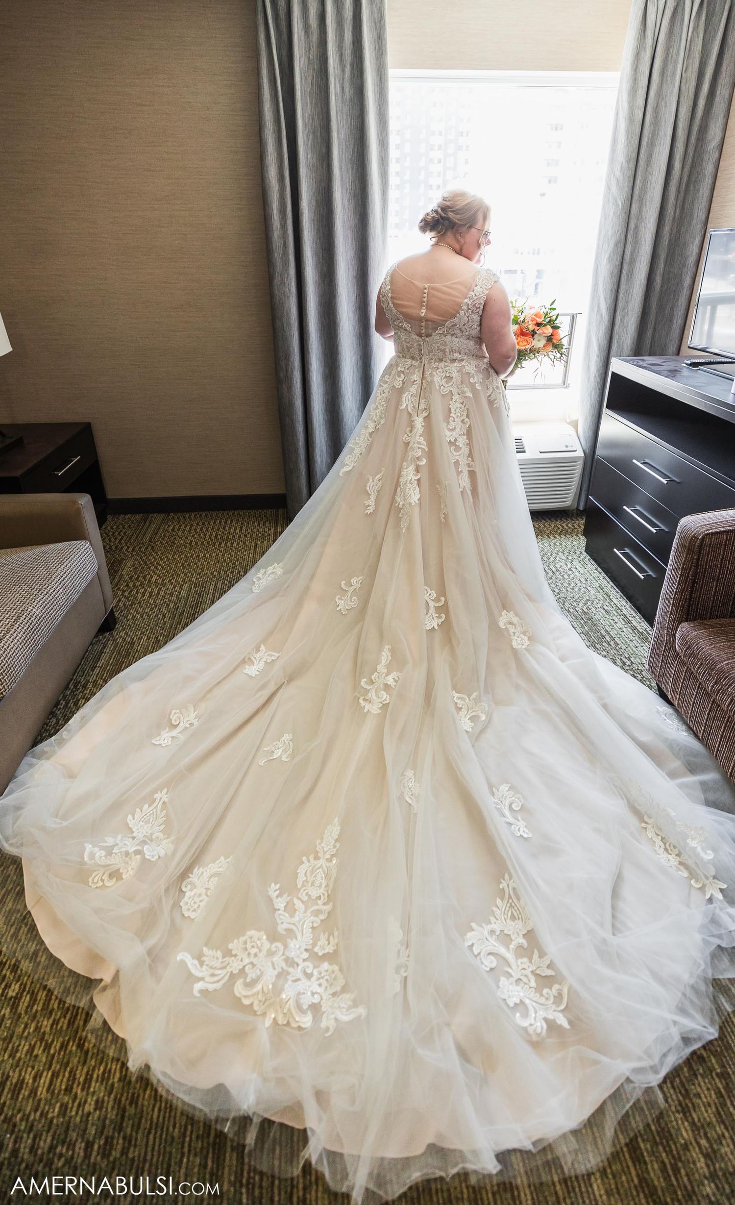Stunning back view of lace wedding gown with cathedral train in hotel room.