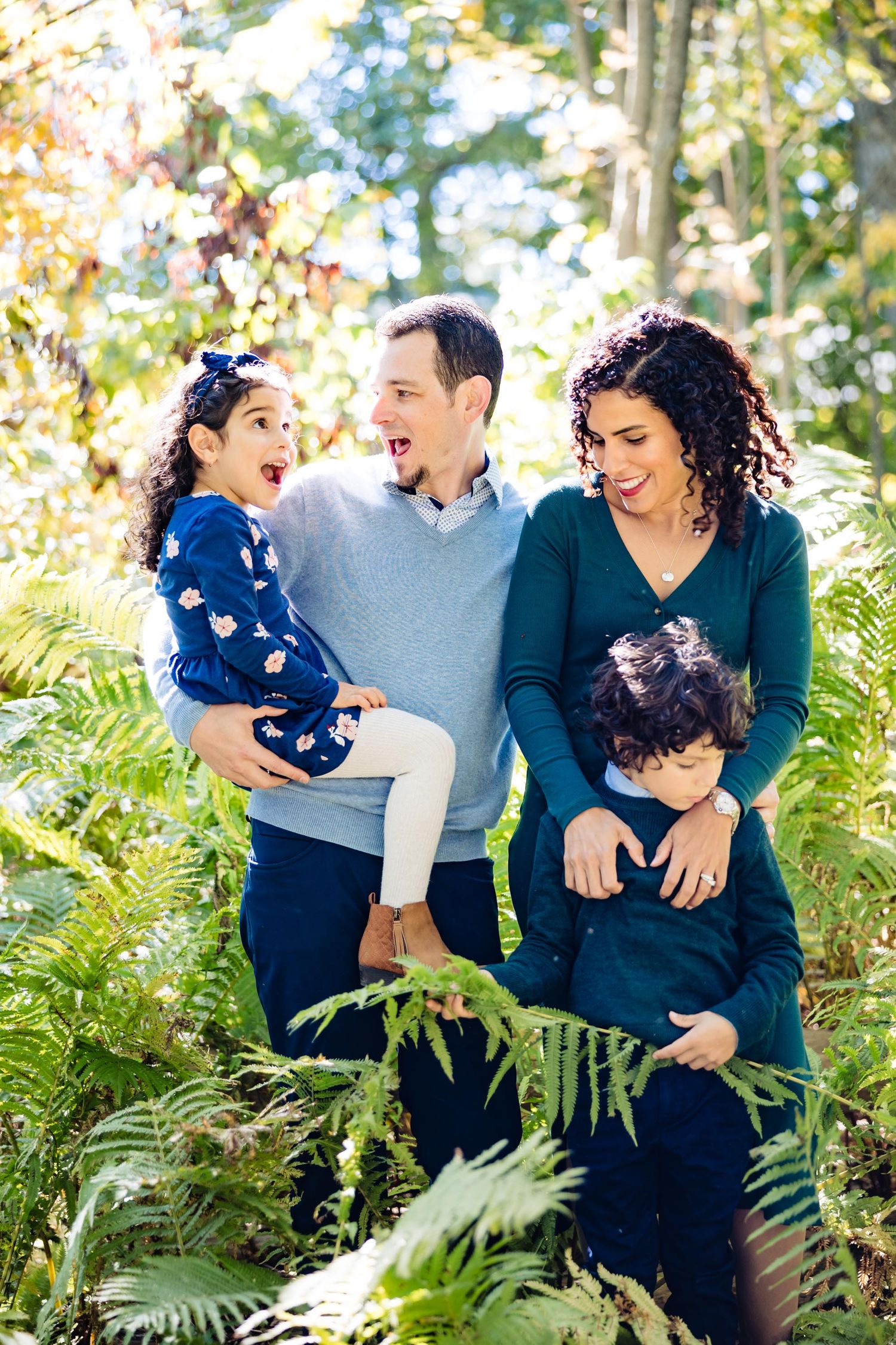 A joyful family moment captured outdoors among ferns and autumn foliage.