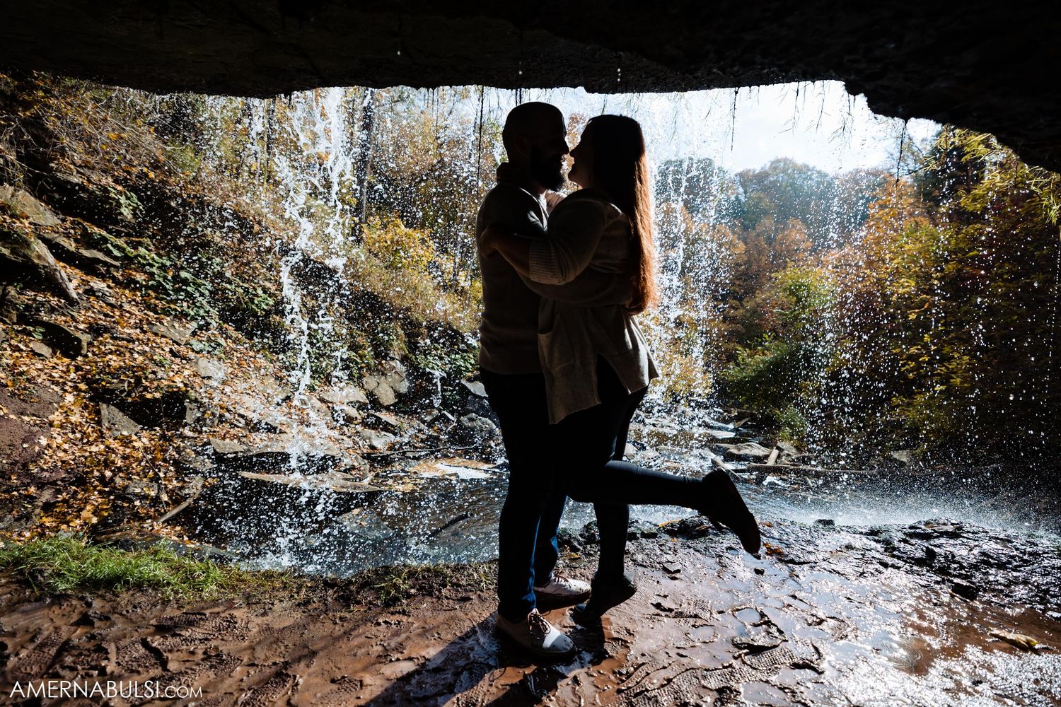 Silhouetted couple sharing intimate moment behind waterfall in cave.