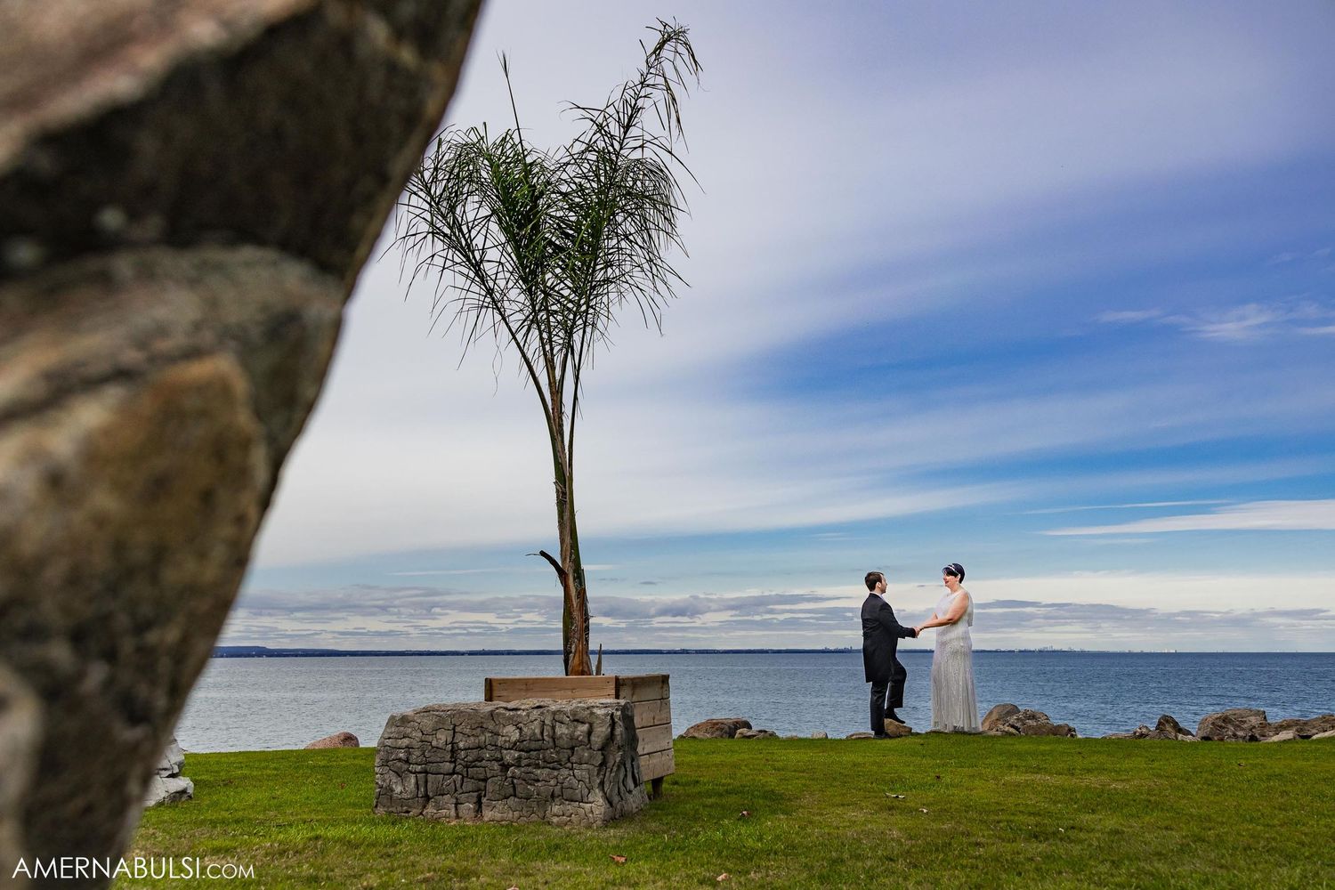 Scenic waterfront wedding ceremony setup with a lone palm tree against blue skies.