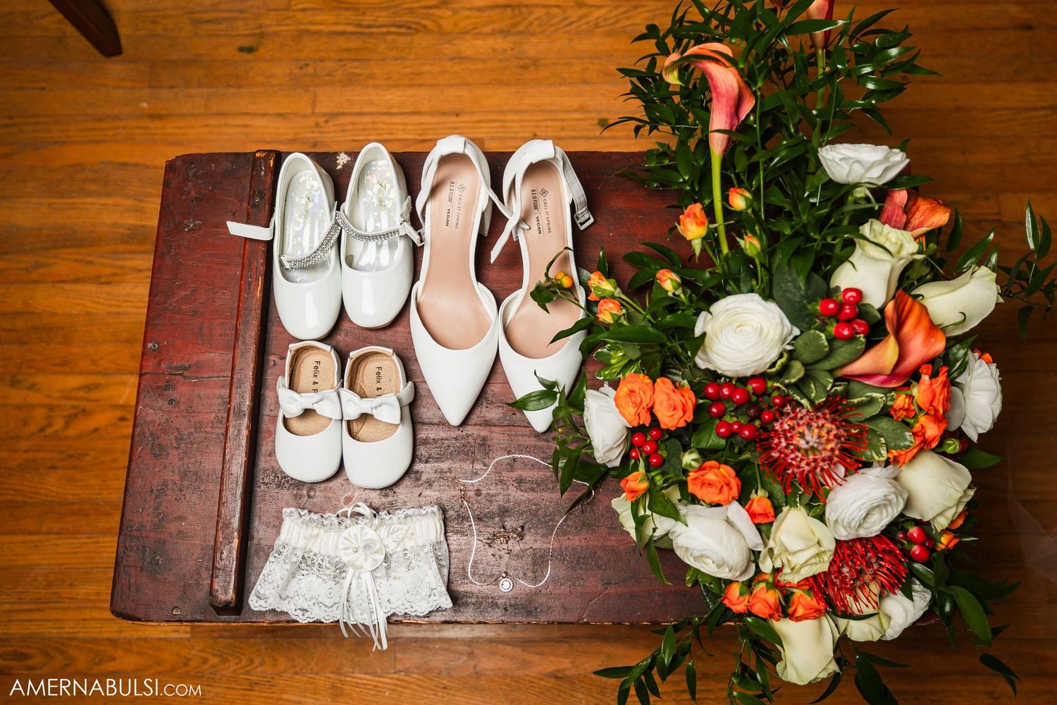 Wedding shoes and floral arrangement with coral and white flowers on wooden surface.