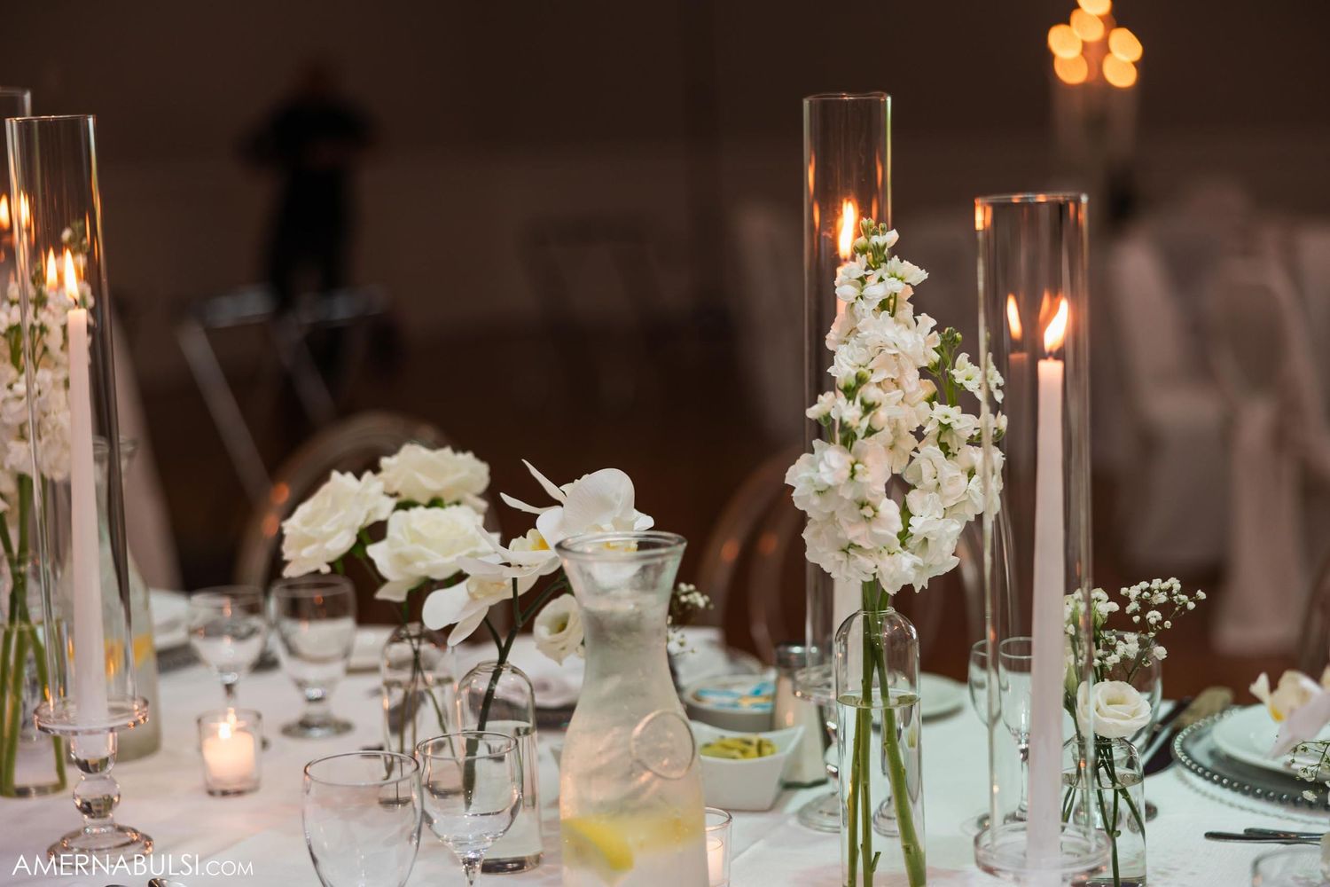 Elegant white floral centerpieces with tall candle holders on wedding reception table.
