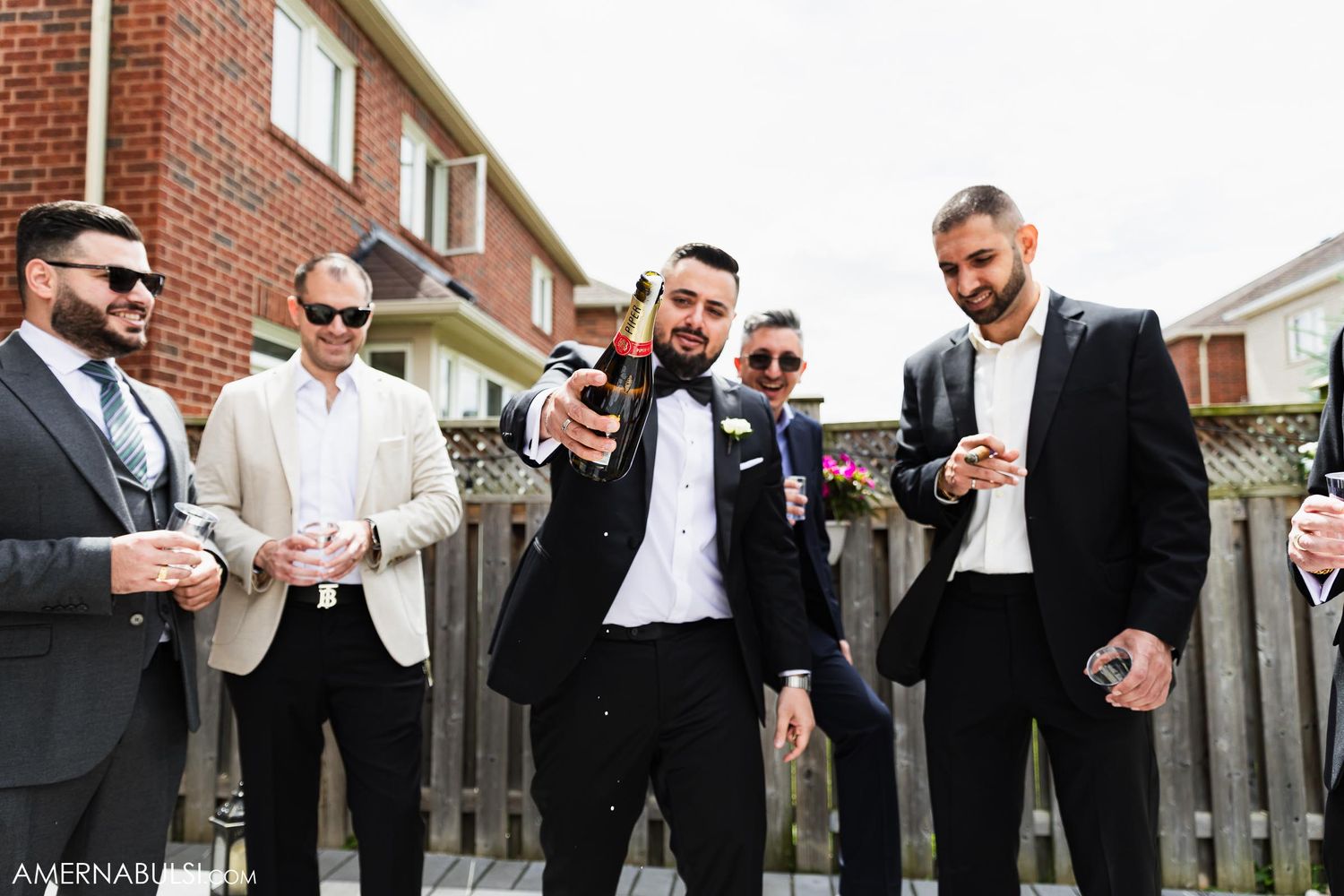 Groomsmen in formal attire sharing a lighthearted moment outdoors.