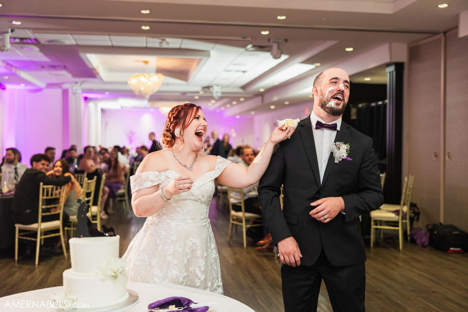 Newlyweds laughing together during cake cutting ceremony at reception.