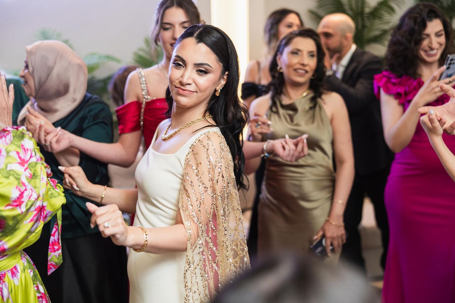 Wedding guests in colorful formal attire dance and celebrate at a festive reception.