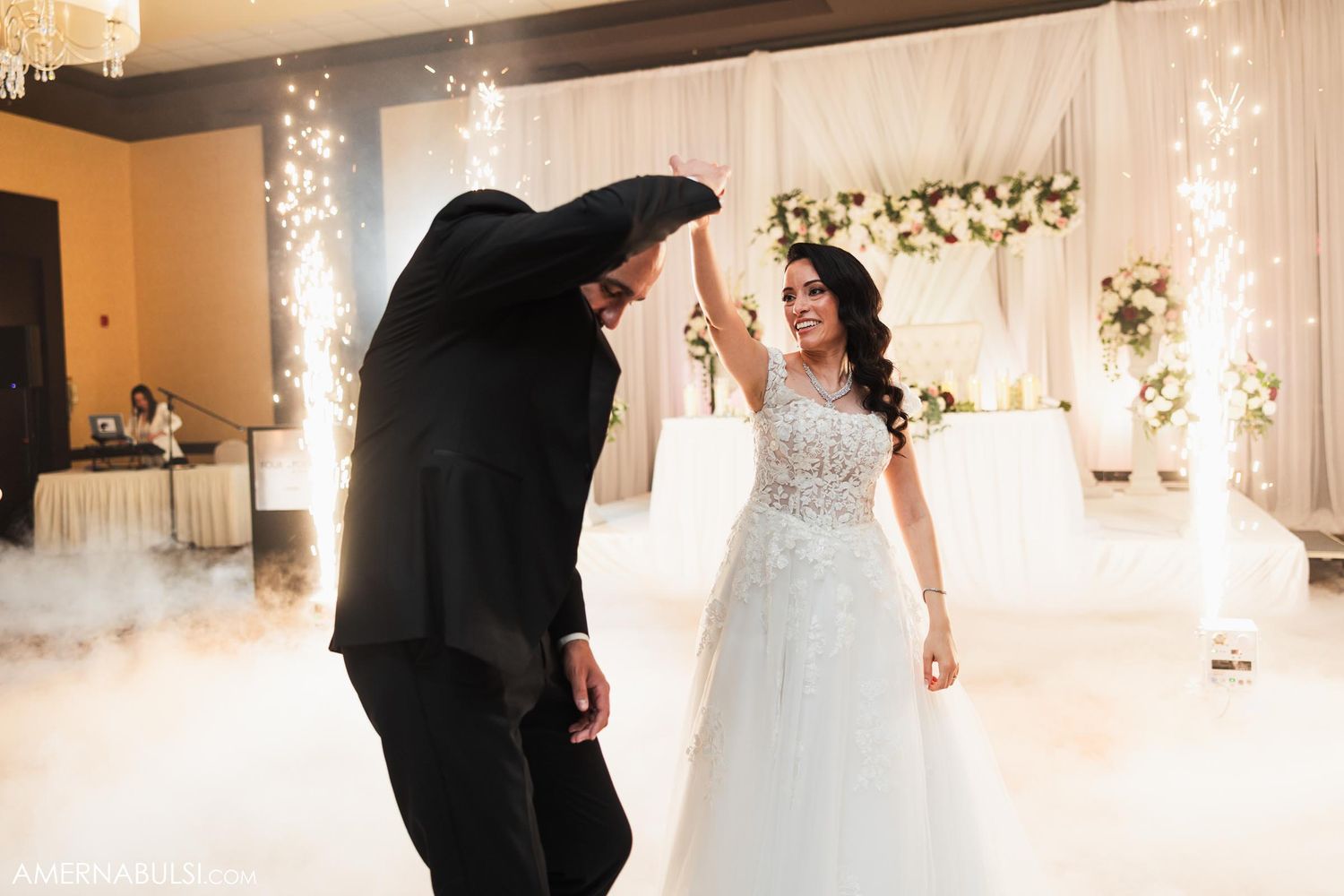 A couple dancing in an elegantly decorated wedding reception hall with twinkling lights and floral decor.