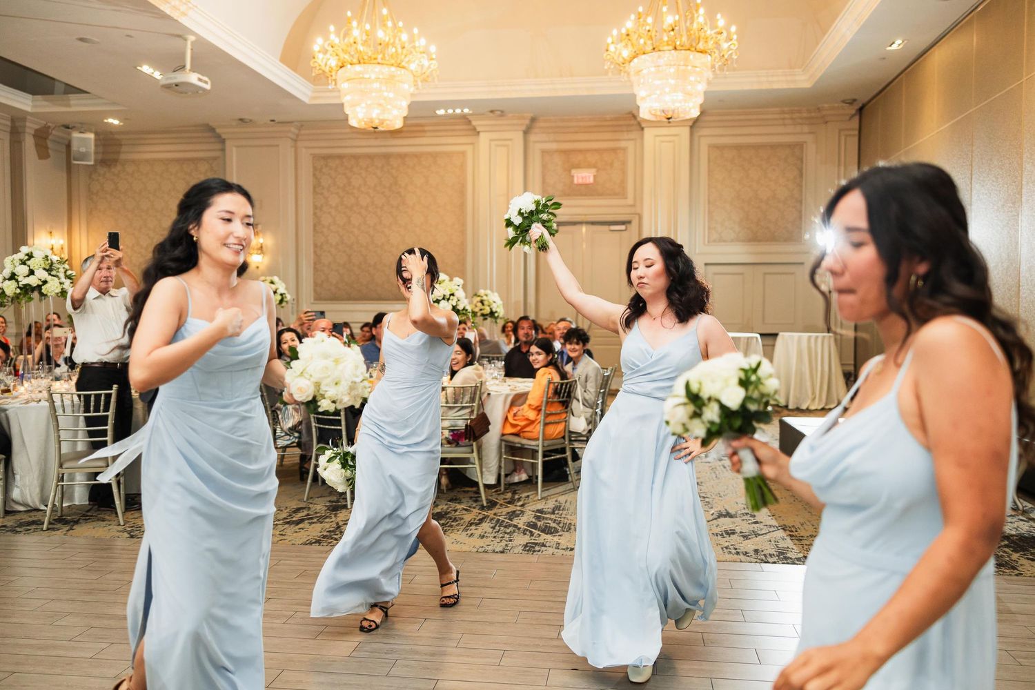 Bridesmaids in light blue dresses dance joyfully during wedding reception.