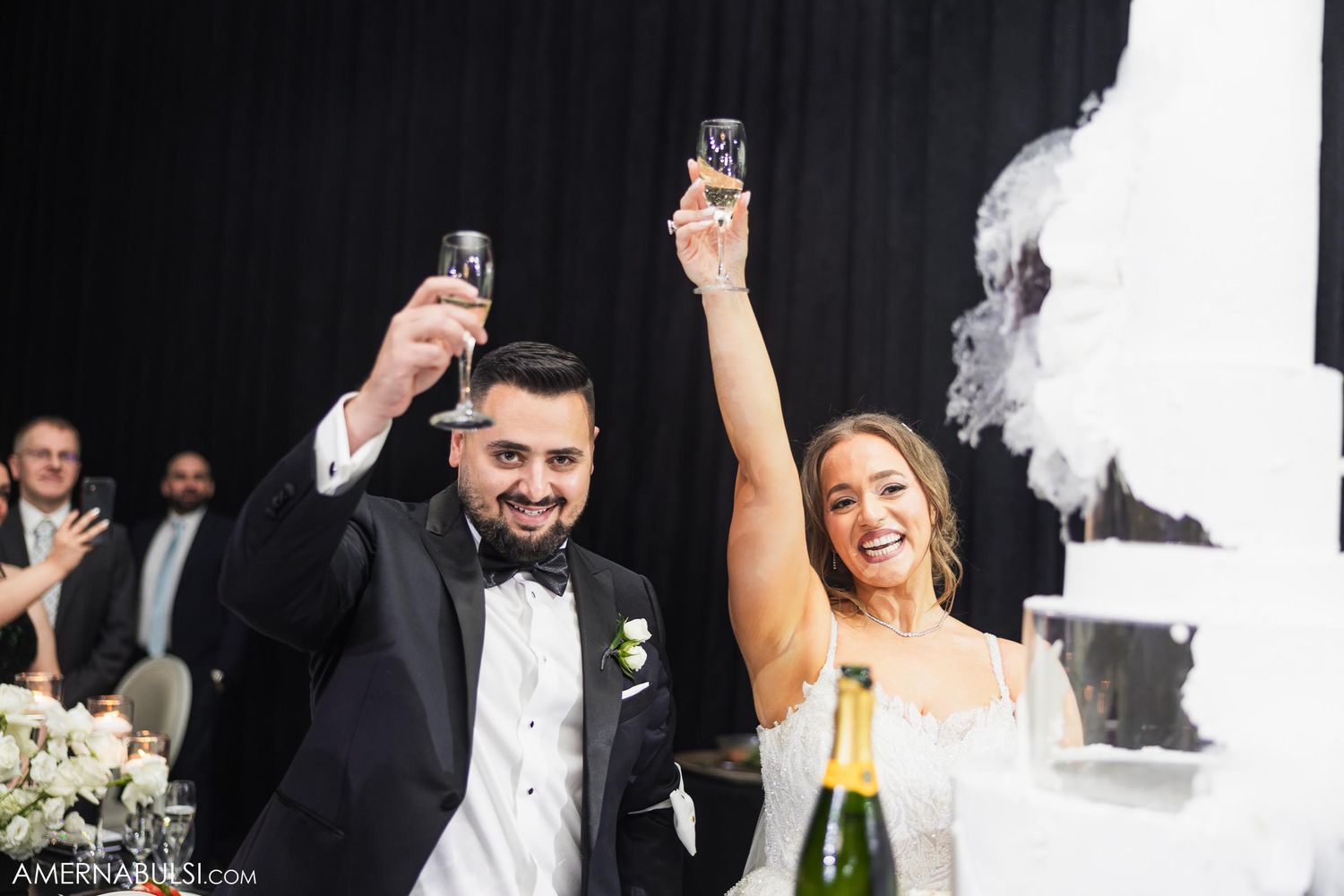 Bride and groom raise champagne glasses in celebration during wedding reception.