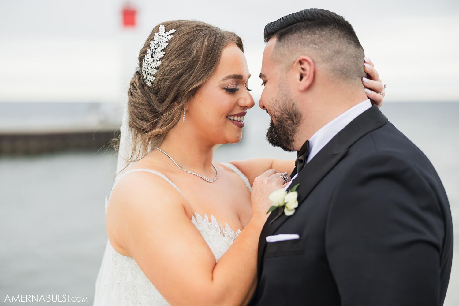 A tender close-up moment between newlyweds with elegant bridal accessories against a waterfront backdrop.