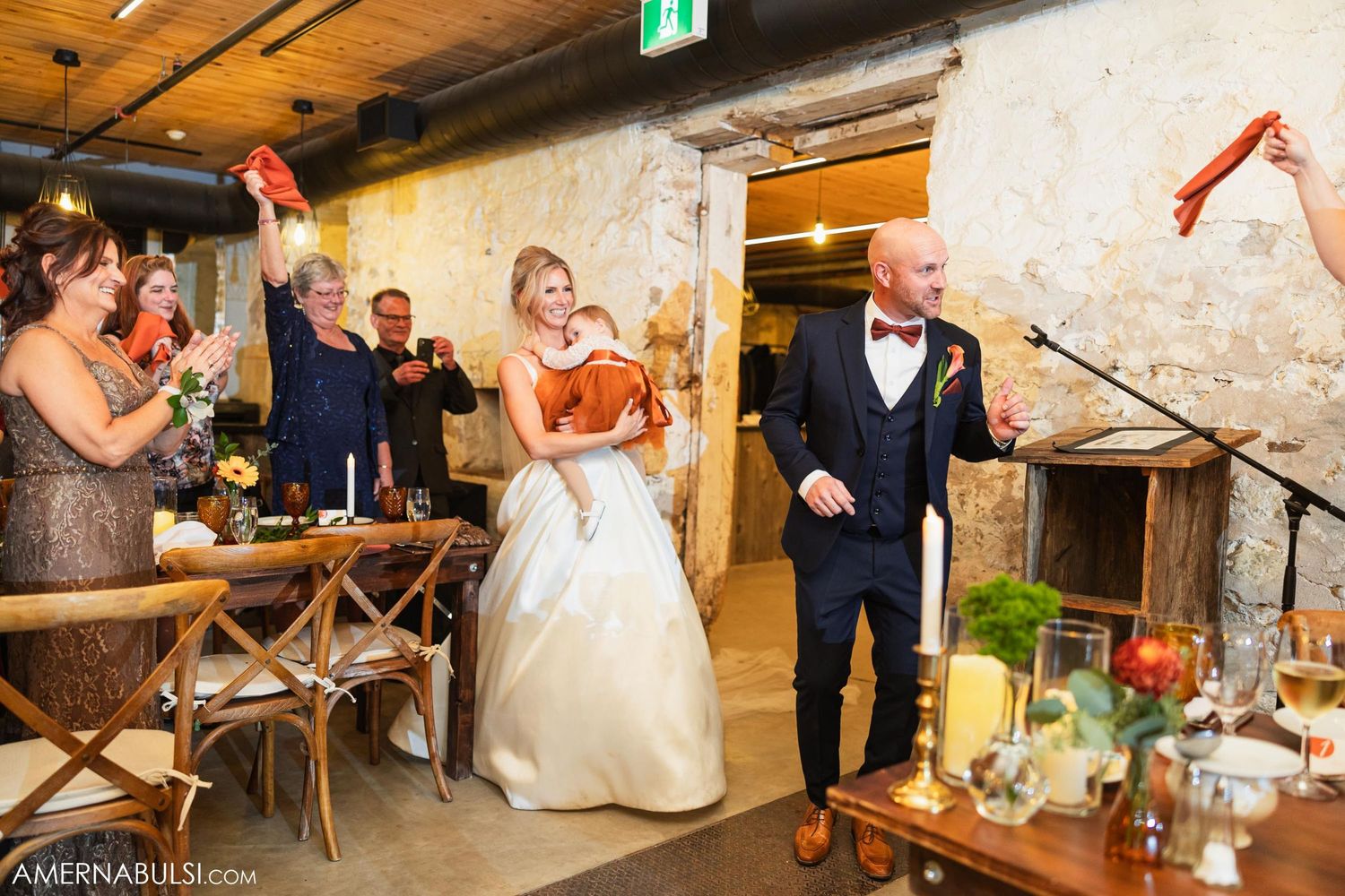 Wedding celebration in rustic venue with guests raising napkins in celebration.