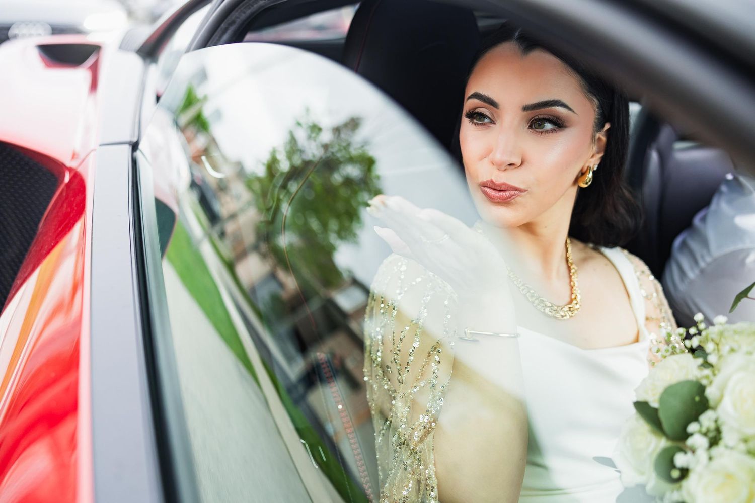 Elegant bride sitting in car with white bouquet and ornate dress.