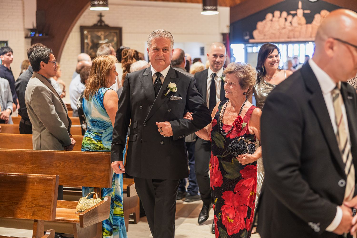 Elegantly dressed wedding guests walk through church aisle following a formal wedding ceremony.
