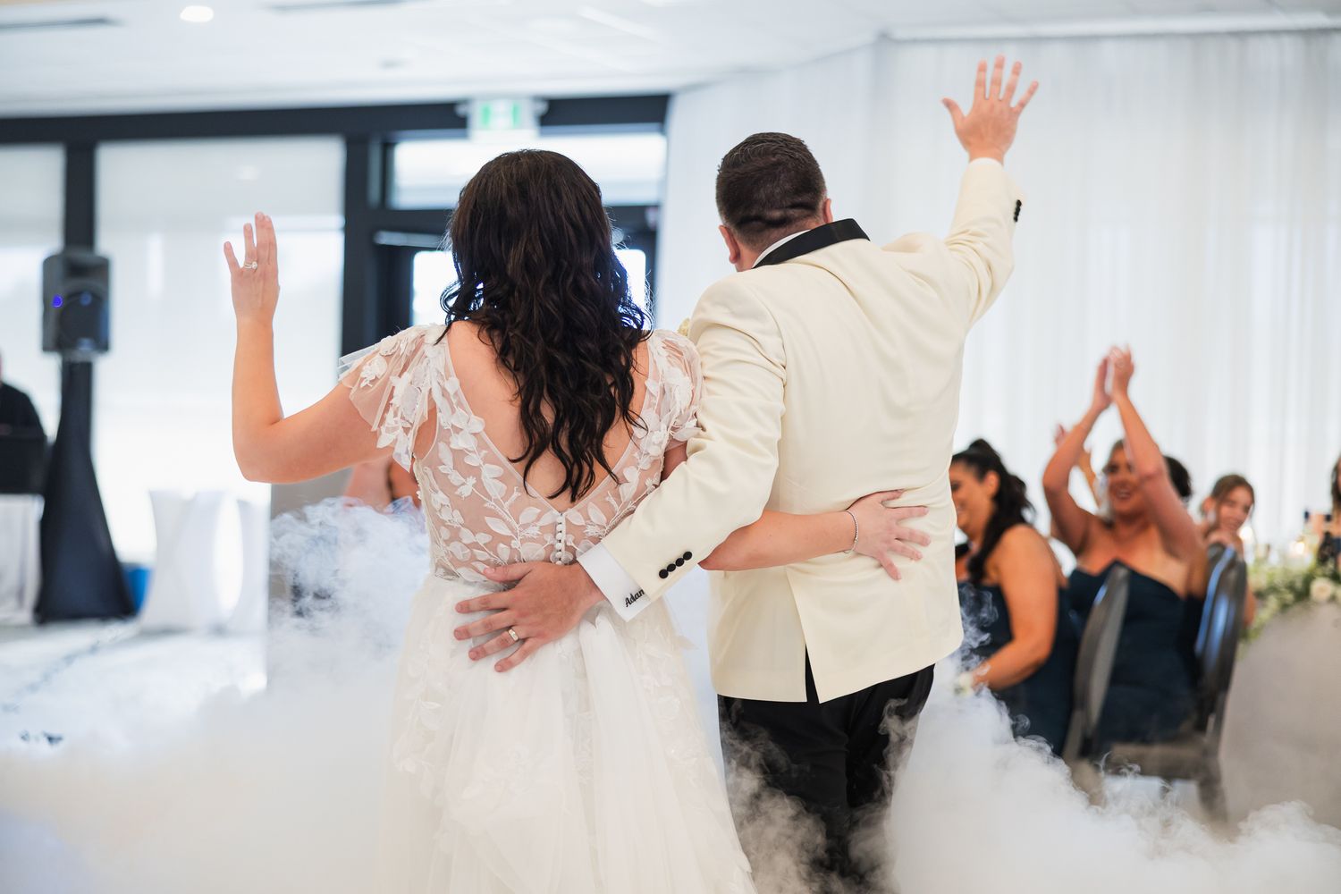 Bride and groom raise hands during first dance surrounded by dramatic fog effect at wedding reception.