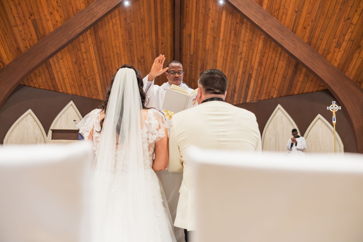 Wedding ceremony in wooden chapel as officiant raises hand blessing bride and groom at the altar.