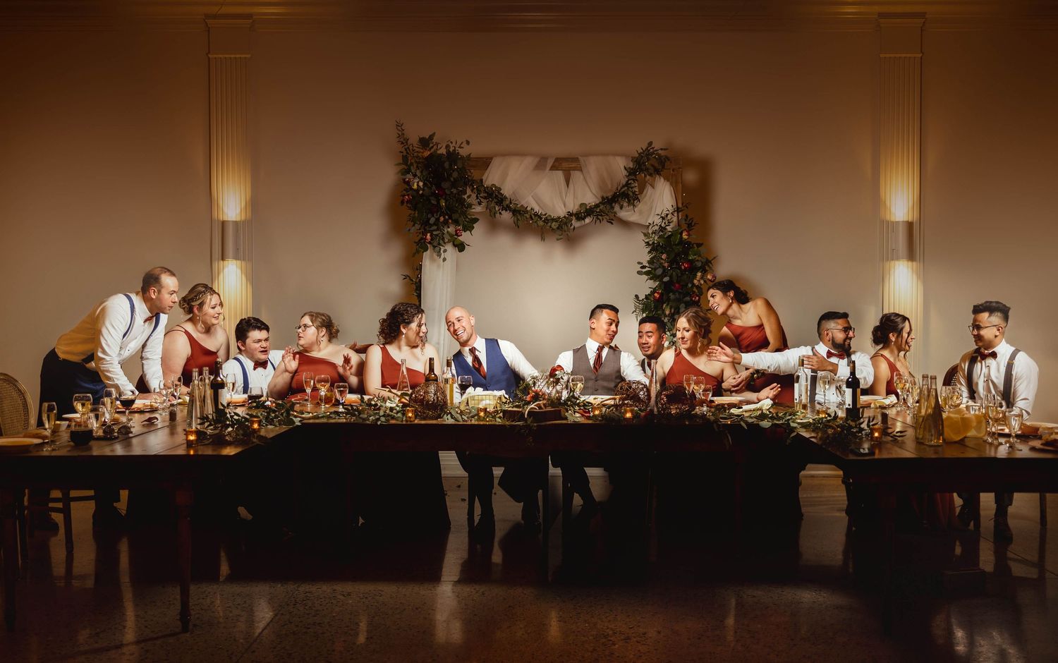Wedding party seated at long rustic table with floral decorations in a recreation of The Last Supper.