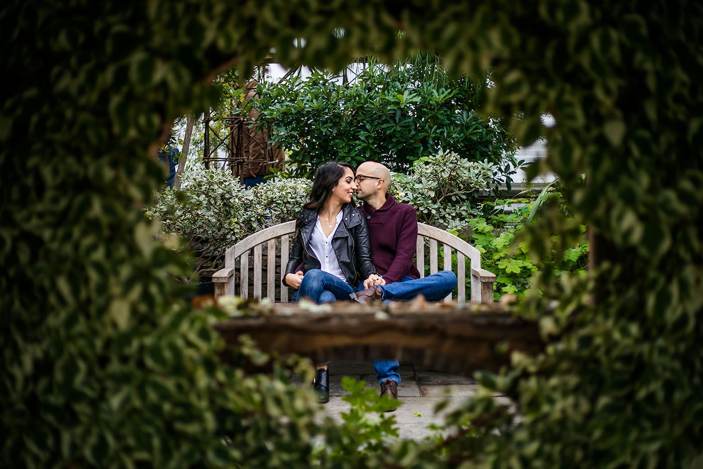 Garden engagement session with natural framing through green leaves.