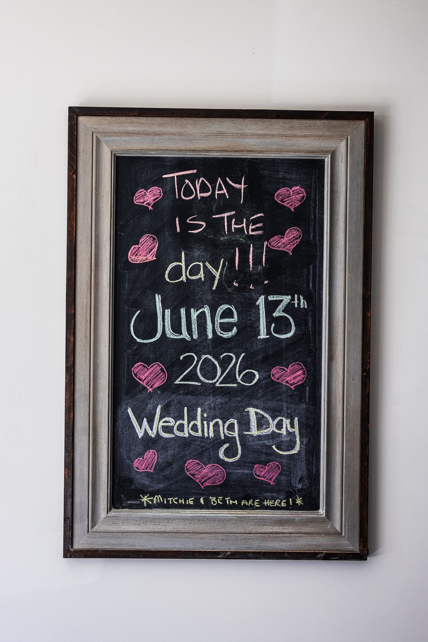 Chalkboard sign in wooden frame reading Today is the Day June 13th 2026 Wedding Day with pink heart decorations.
