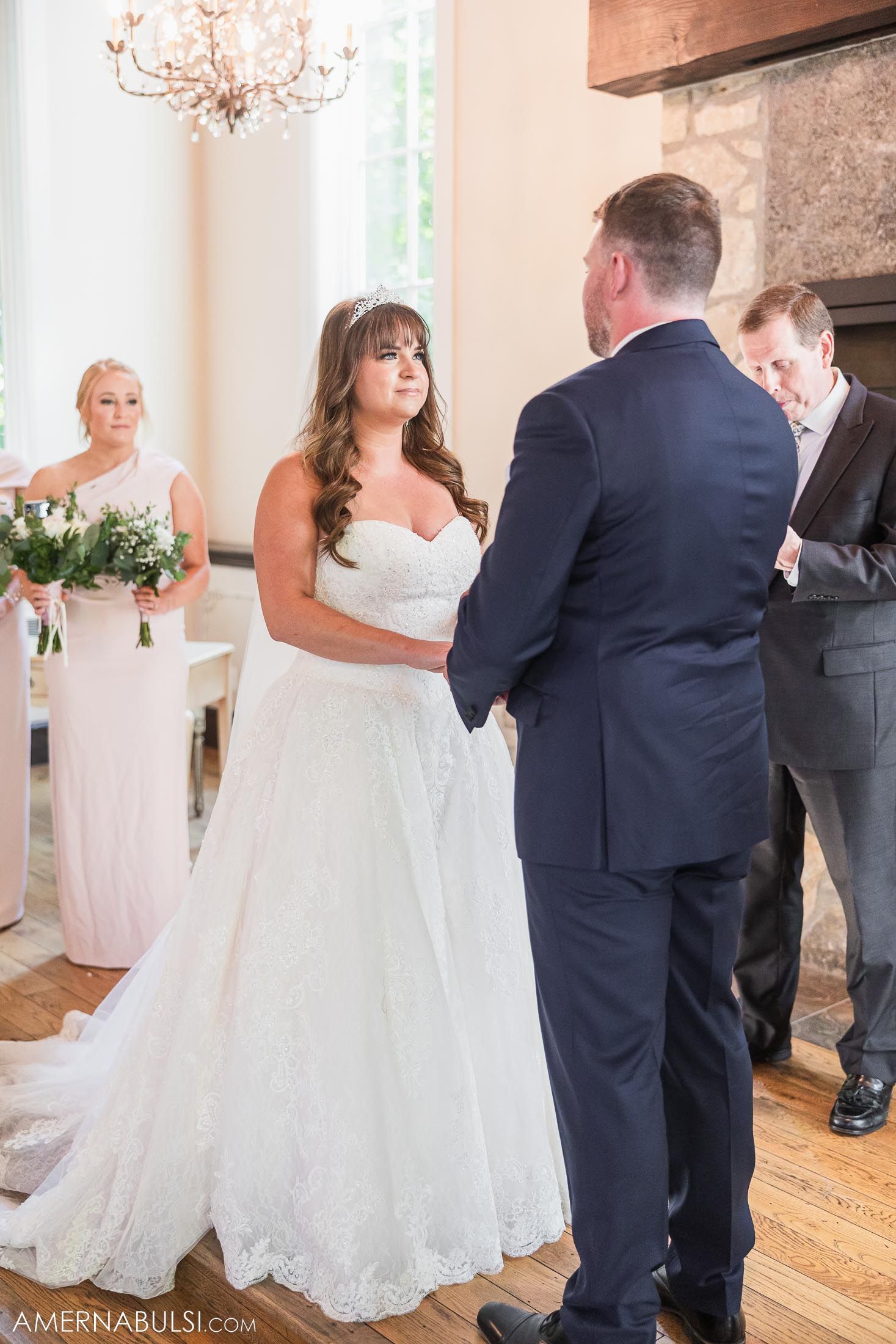 Bride in white gown exchanges vows during ceremony under crystal chandelier.