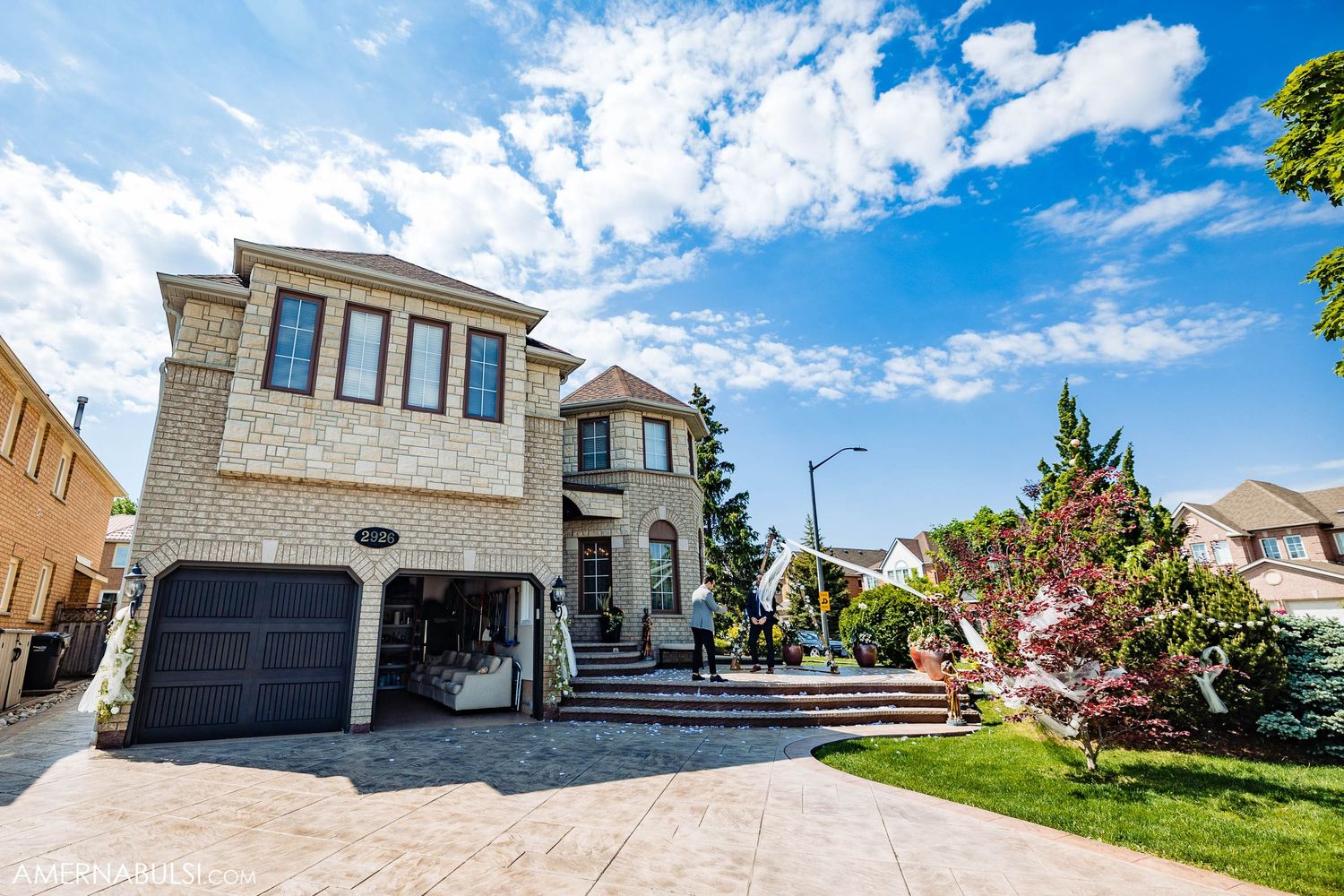 Modern two-story luxury stone house with dark garage door and manicured lawn.