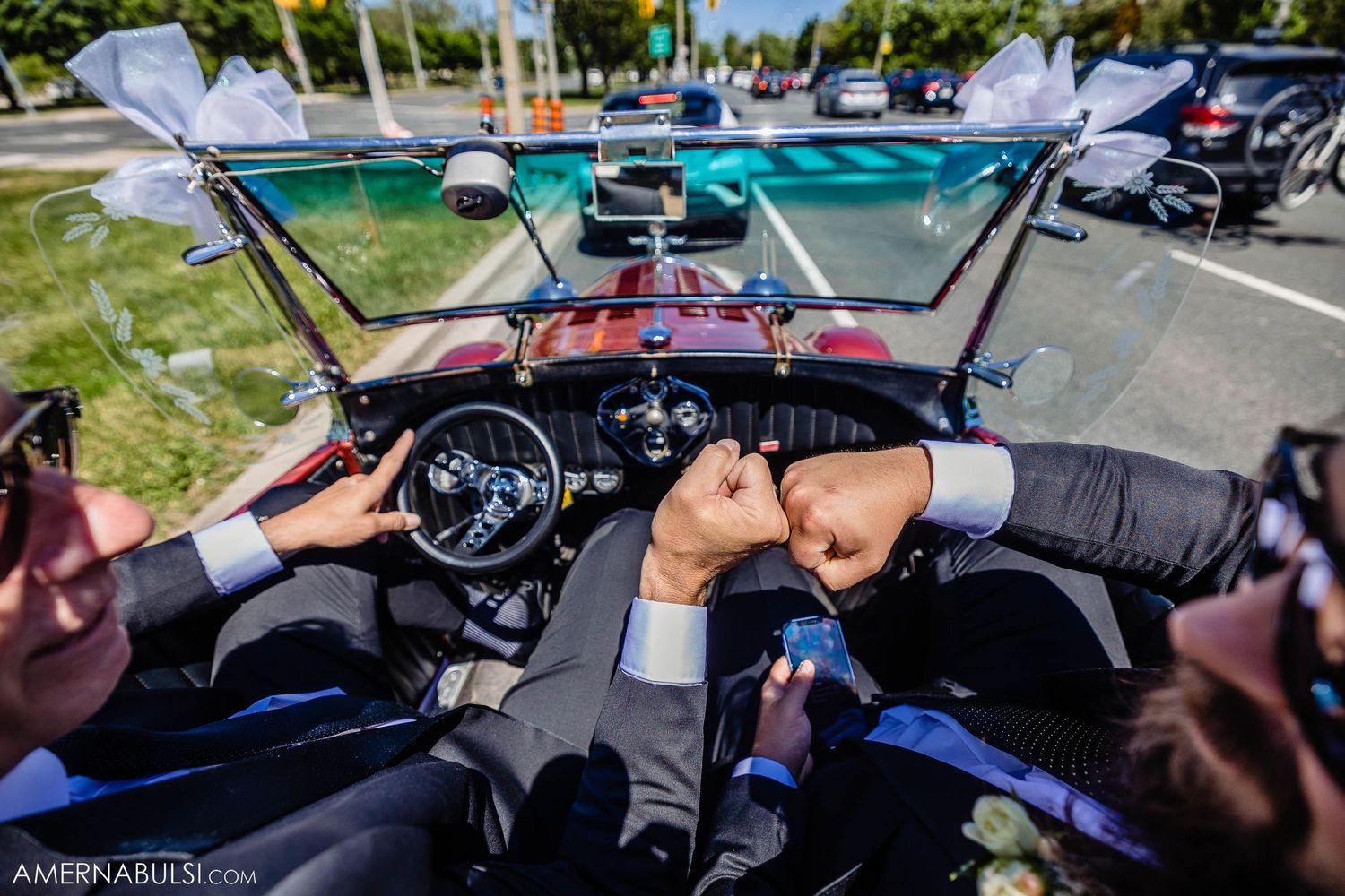Multiple hands grip steering wheel of classic car during wedding day drive.