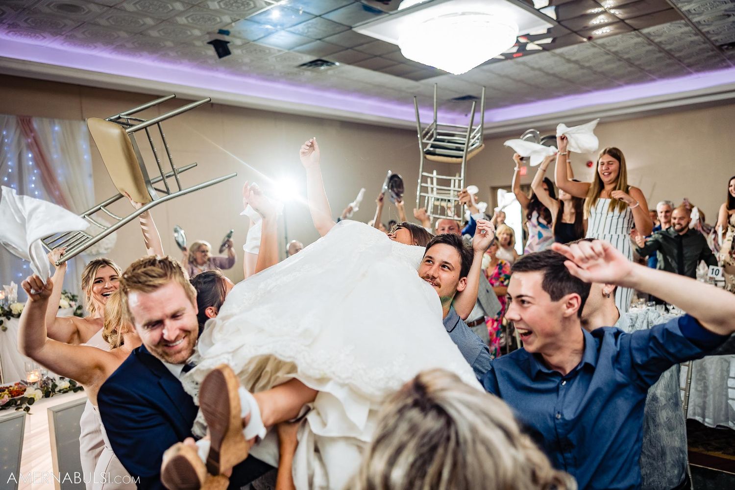 Wedding guests enthusiastically lifting and celebrating during a lively reception dance moment.