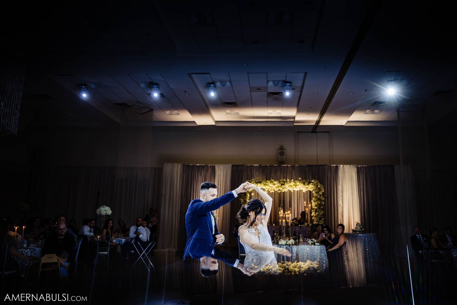 Romantic silhouette of newlyweds dancing under dramatic spotlights at their wedding reception.