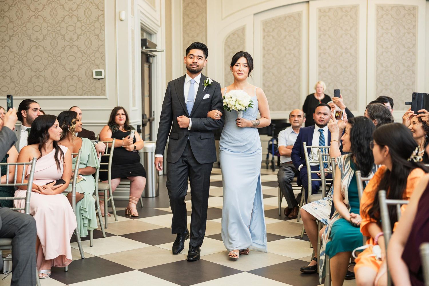 Wedding party members walk down black and white checkered aisle during ceremony processional.
