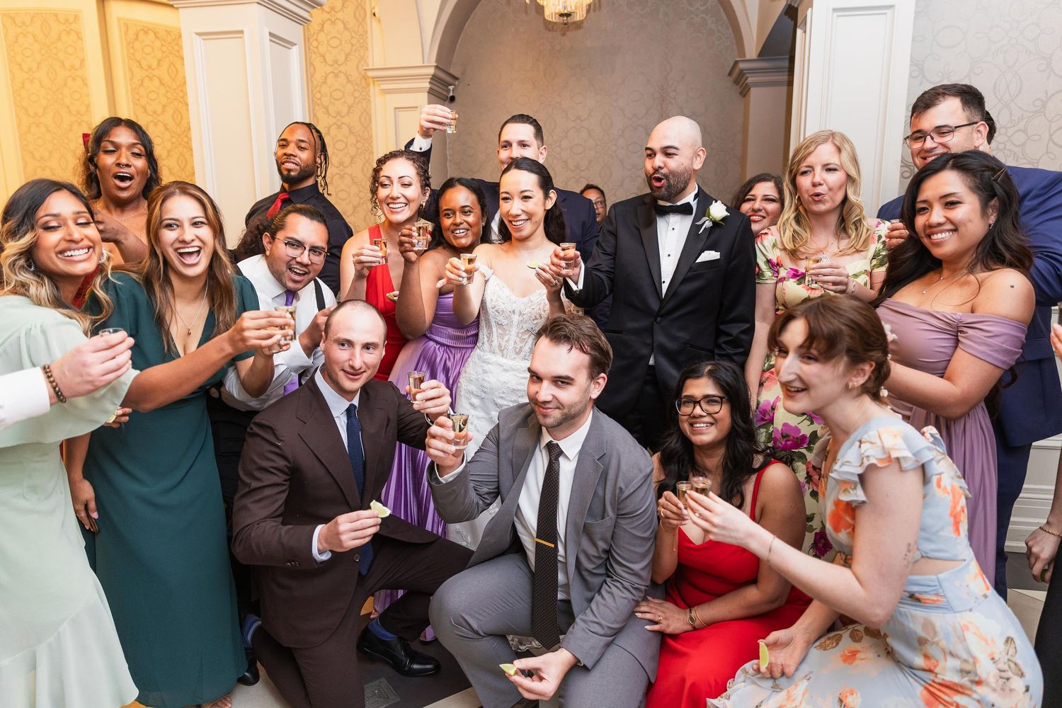 Large wedding party group poses together for fun celebratory photo at elegant venue.