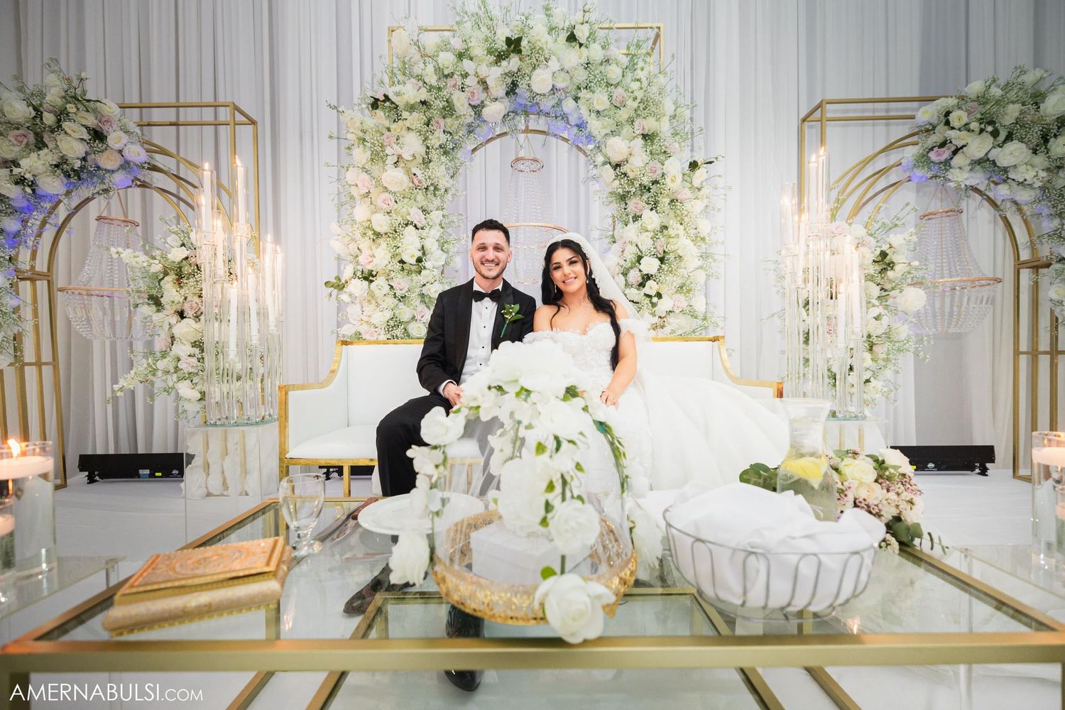 Elegant wedding reception setup with white floral arches and golden geometric decor elements.
