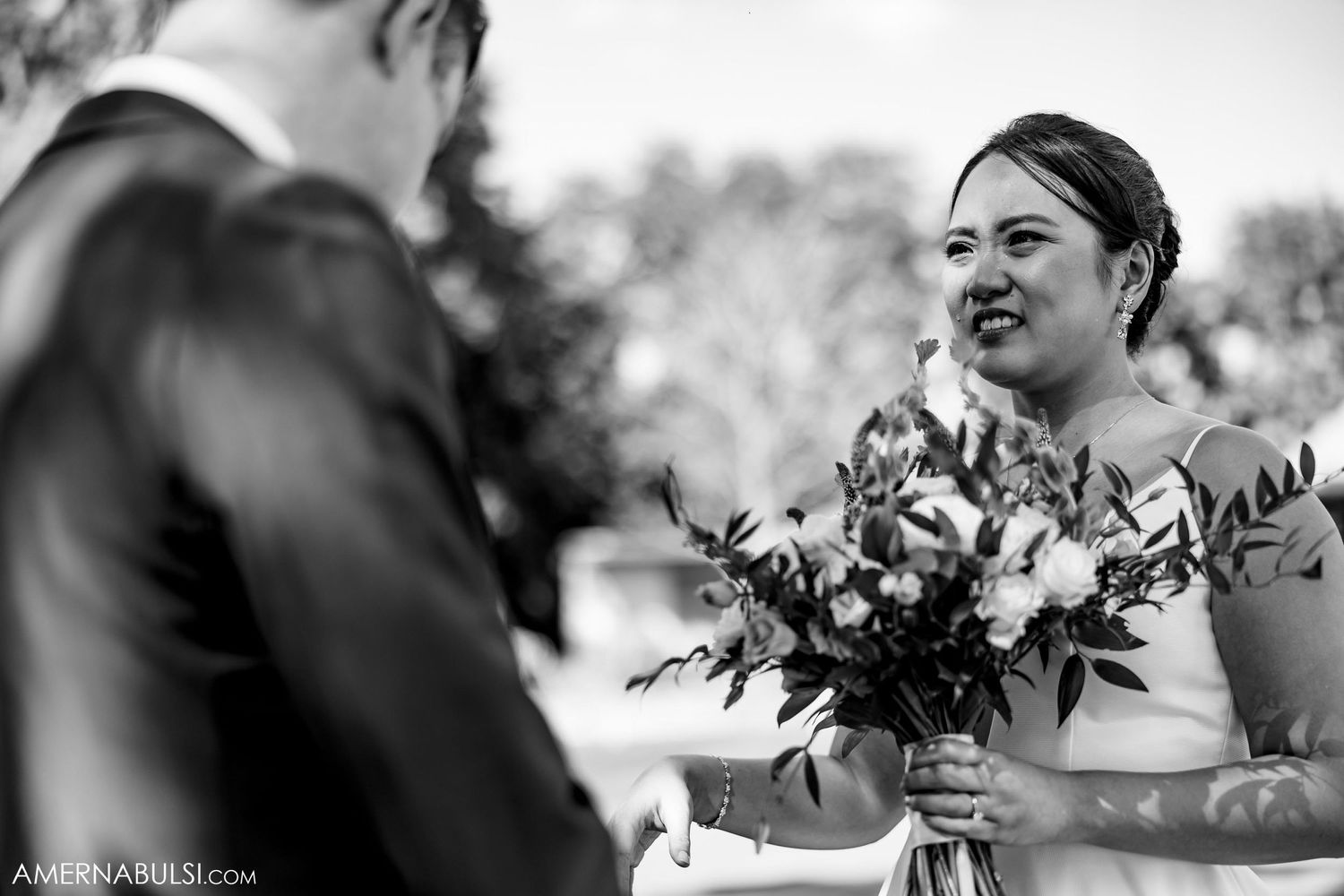 Black and white photo of a joyful couple sharing laughter during their wedding ceremony with floral bouquet.