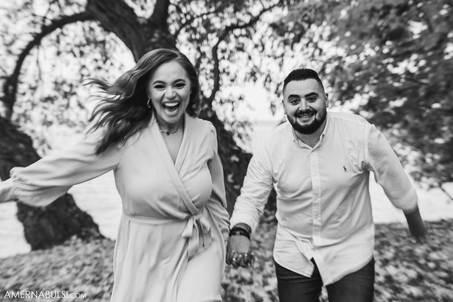 A joyful couple running and laughing together in a casual outdoor setting during an autumn photo session.