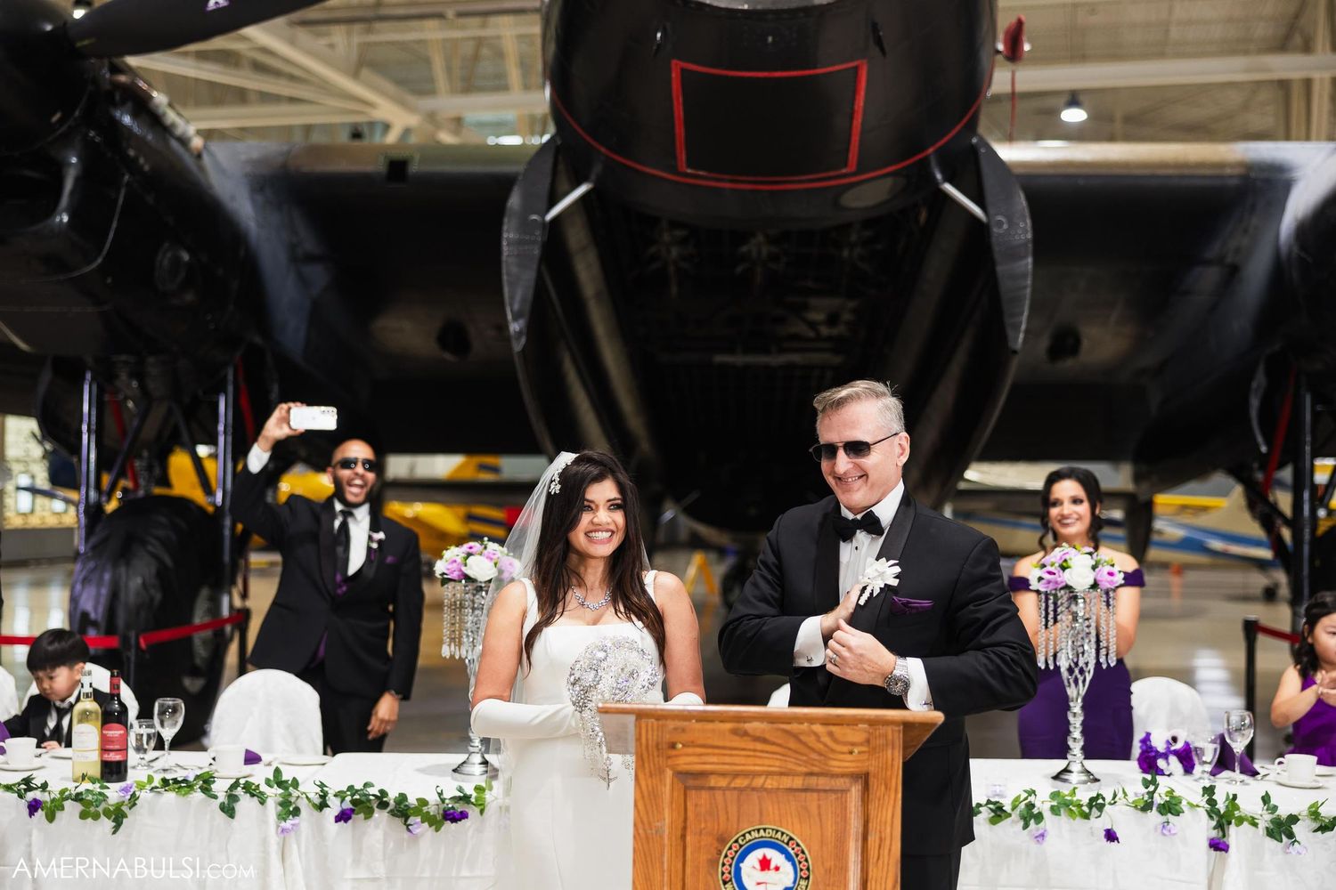 Wedding ceremony setup in aircraft hangar with vintage plane backdrop and floral decorations.