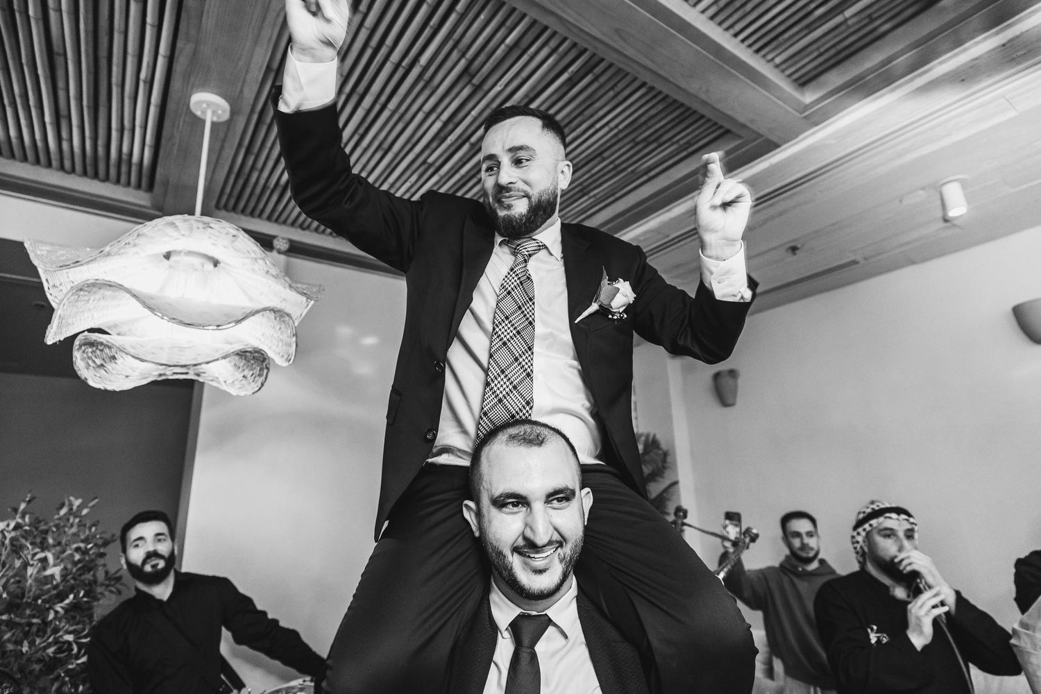 Wedding celebration with guests cheering during traditional lift celebration.