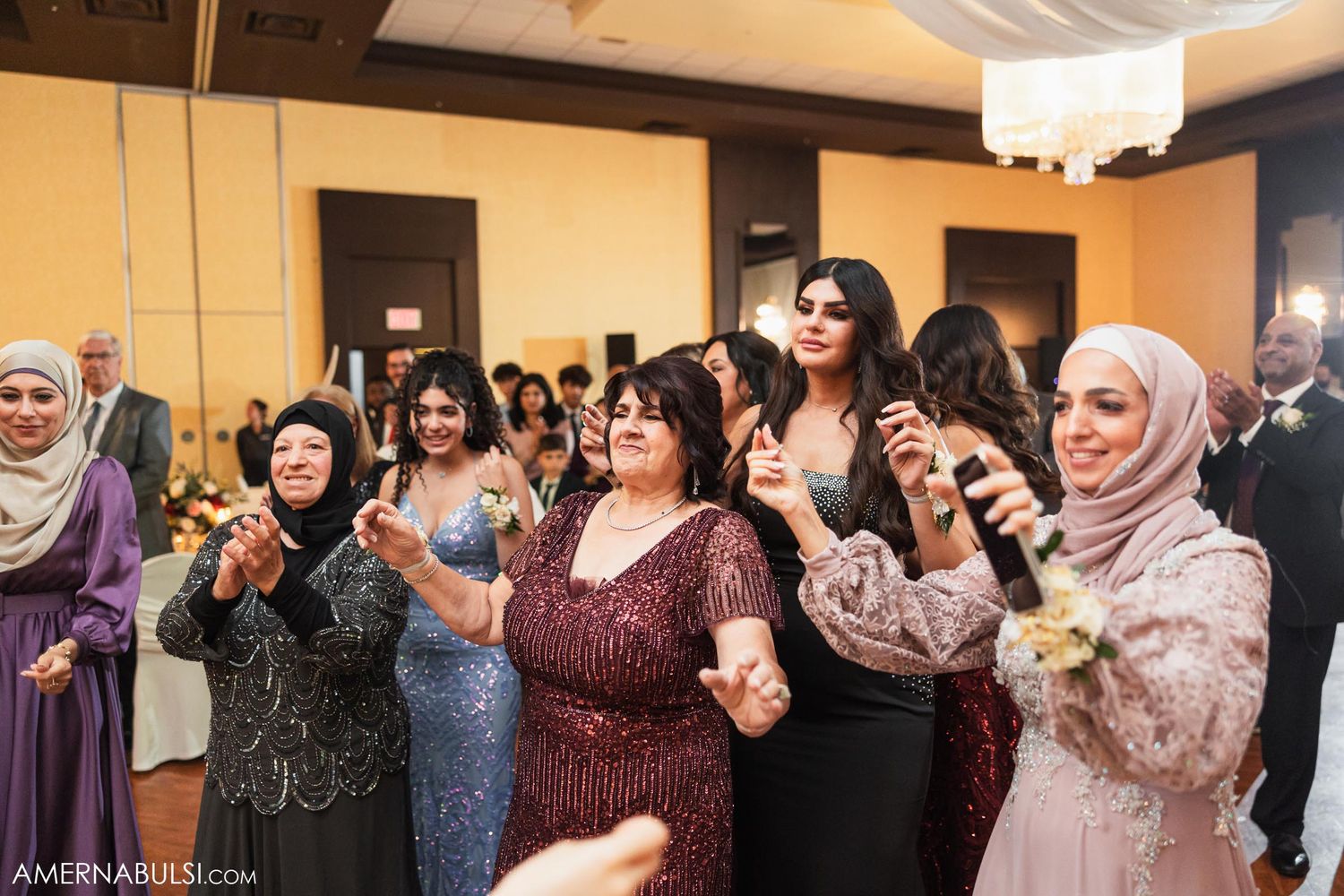 Wedding guests dancing and celebrating with joy in a banquet hall with warm lighting.
