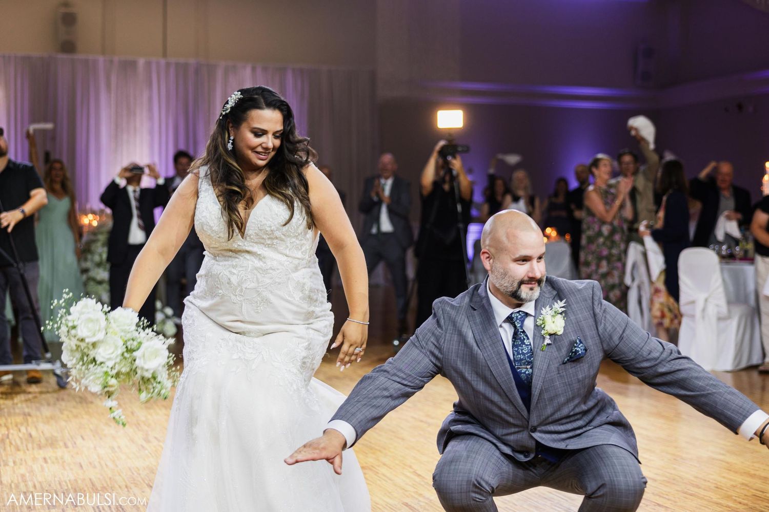 Playful dance moves performed during wedding celebration in elegant ballroom setting.