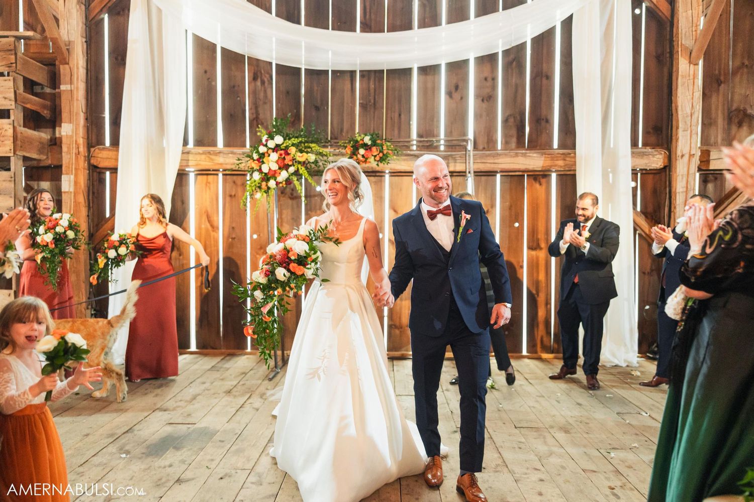 Newlyweds celebrate while walking down aisle in beautifully decorated barn venue.