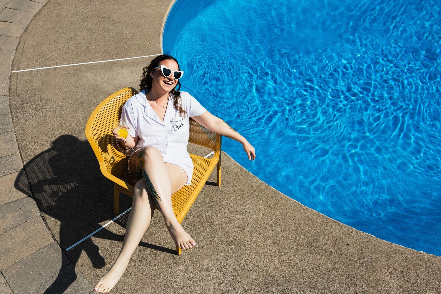 Person lounging in yellow chair beside blue swimming pool wearing sunglasses.