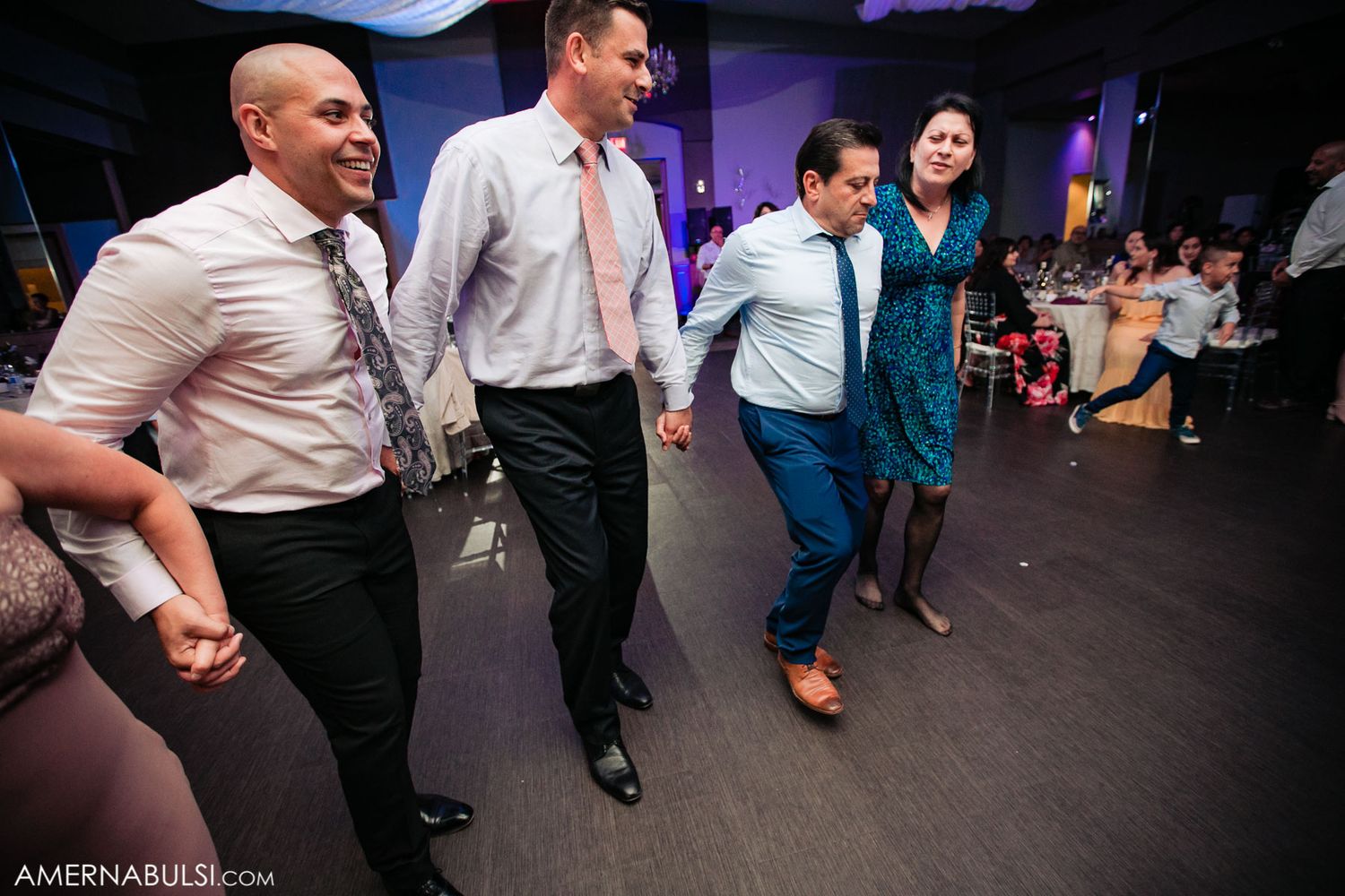 Wedding guests dance and celebrate on a dimly lit dance floor at a reception party.