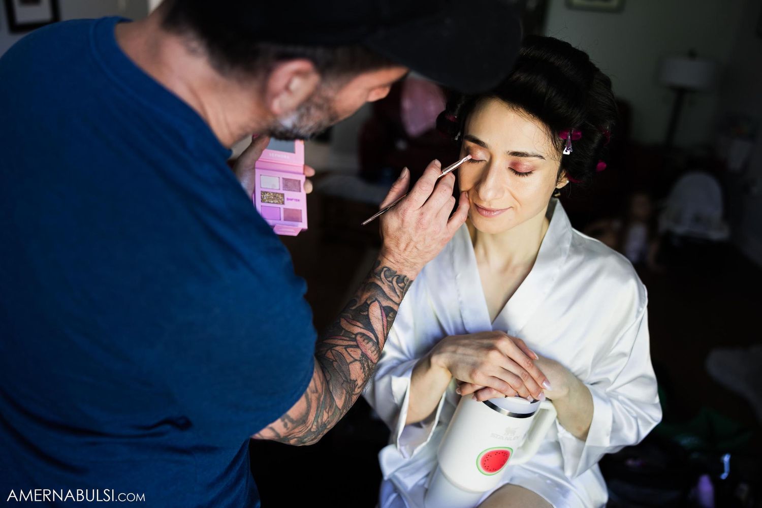A makeup artist applies cosmetics to someone wearing a white robe during preparation.