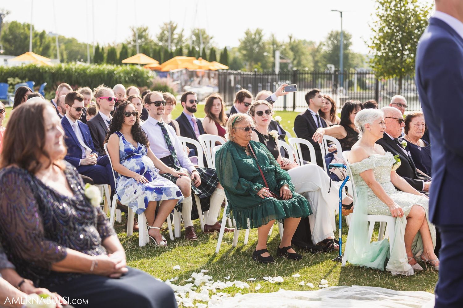 Wedding guests seated on white chairs on a grassy lawn during an outdoor ceremony.